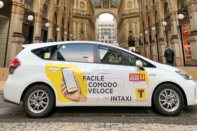 Taxi bianco con la scritta “Facile, Comodo, Veloce” parcheggiato in uno storico porticato europeo con architettura decorata e pavimentazione in ciottoli.