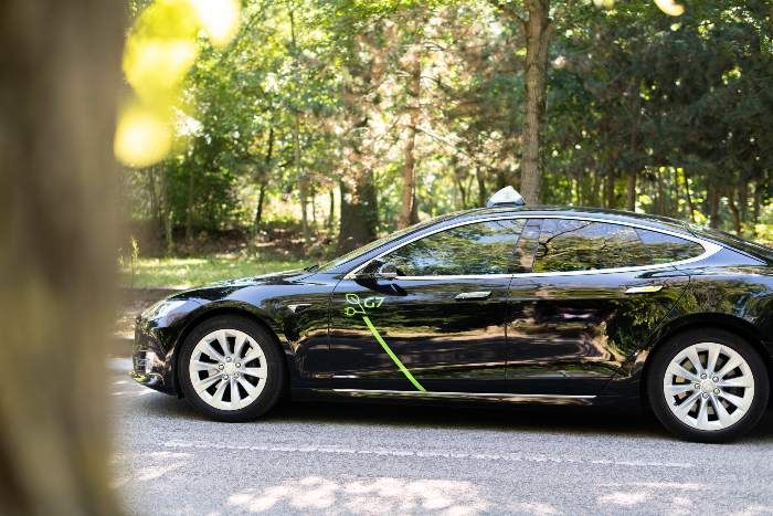 Voiture électrique noire avec des accents verts garée sur une route dans un parc luxuriant et ensoleillé.