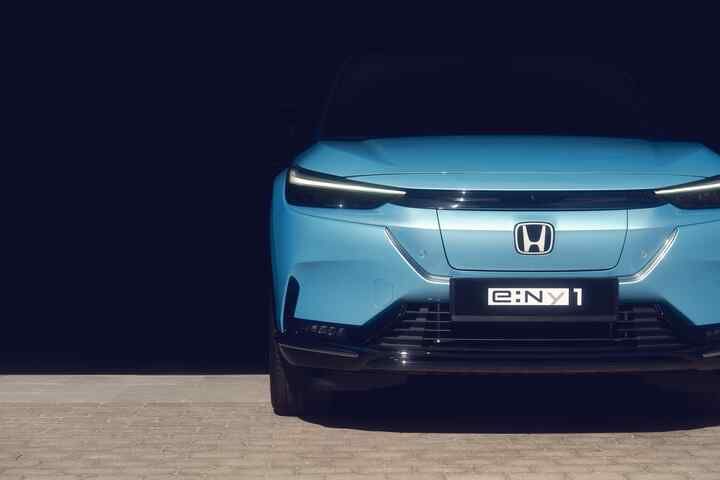 Vista frontale di un'auto elettrica blu Honda e:Ny1 su uno sfondo scuro, che mette in risalto il suo design elegante e i moderni fari.