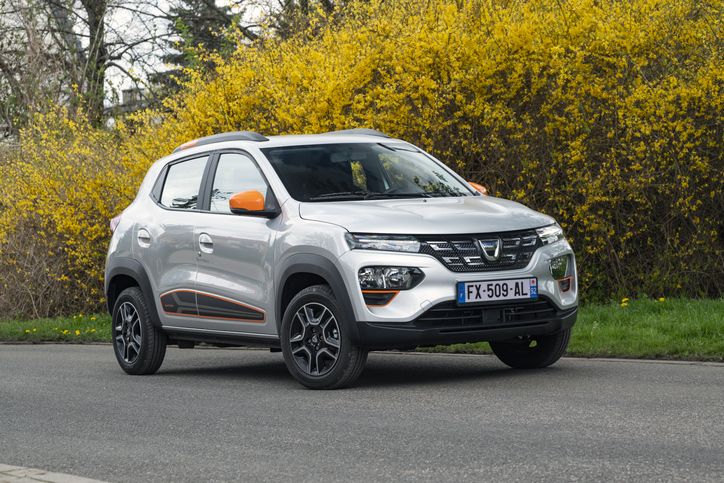 SUV compacto prateado estacionado numa estrada com arbustos floridos amarelos ao fundo; apresenta detalhes em laranja e jantes de liga leve pretas.