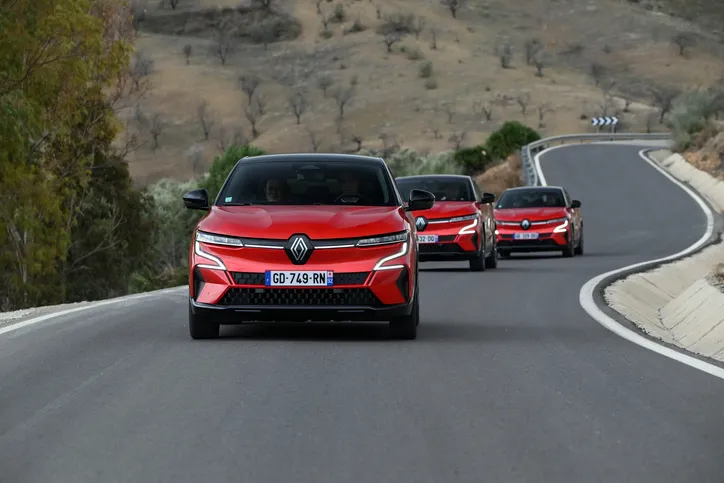 Drei rote Renaults fahren in versetzter Formation auf einer kurvenreichen Straße durch eine hügelige, karge Landschaft.