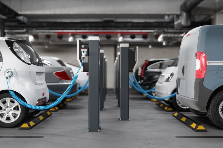 Des véhicules électriques se rechargent à des bornes situées dans un parking souterrain, reliées par des câbles bleus aux points de recharge situés entre les voitures stationnées.