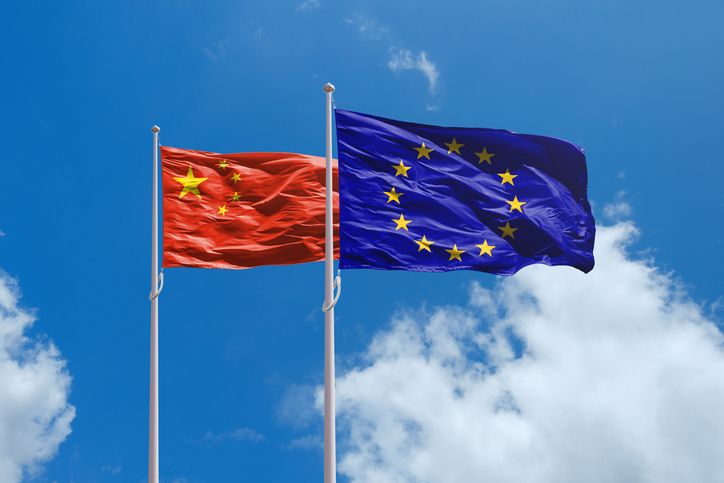 Chinese and European Union flags waving side by side against a blue sky with fluffy clouds.