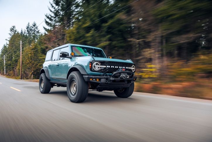 A teal off-road vehicle speeds down a rural road, surrounded by blurred trees.