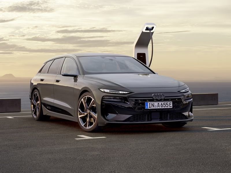 A sleek gray Audi electric car parked at a charging station under a cloudy sky, showcasing modern design and innovation.