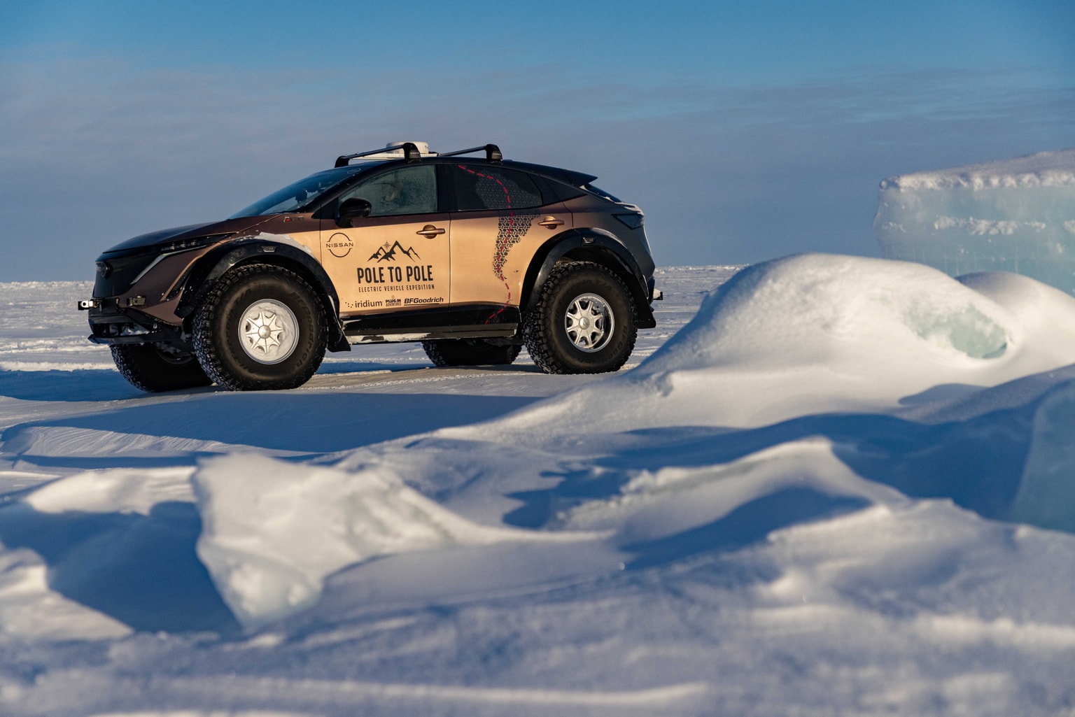 Un veicolo elettrico con la scritta "Pole to Pole" attraversa un paesaggio innevato e ghiacciato sotto un cielo terso e azzurro.