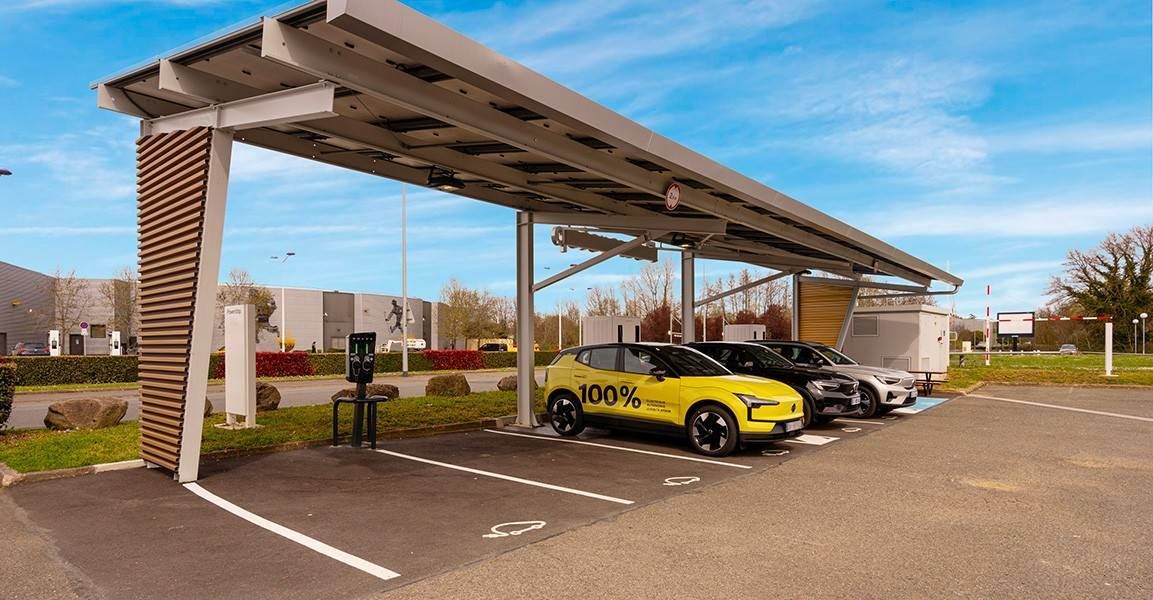 Station de recharge solaire avec trois voitures électriques garées en dessous. La première voiture est jaune vif. Ciel dégagé en arrière-plan.