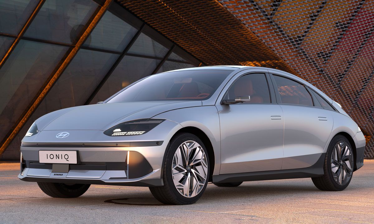 Carro prateado sobre betão com um edifício com grades metálicas ao fundo e tons alaranjados do pôr do sol