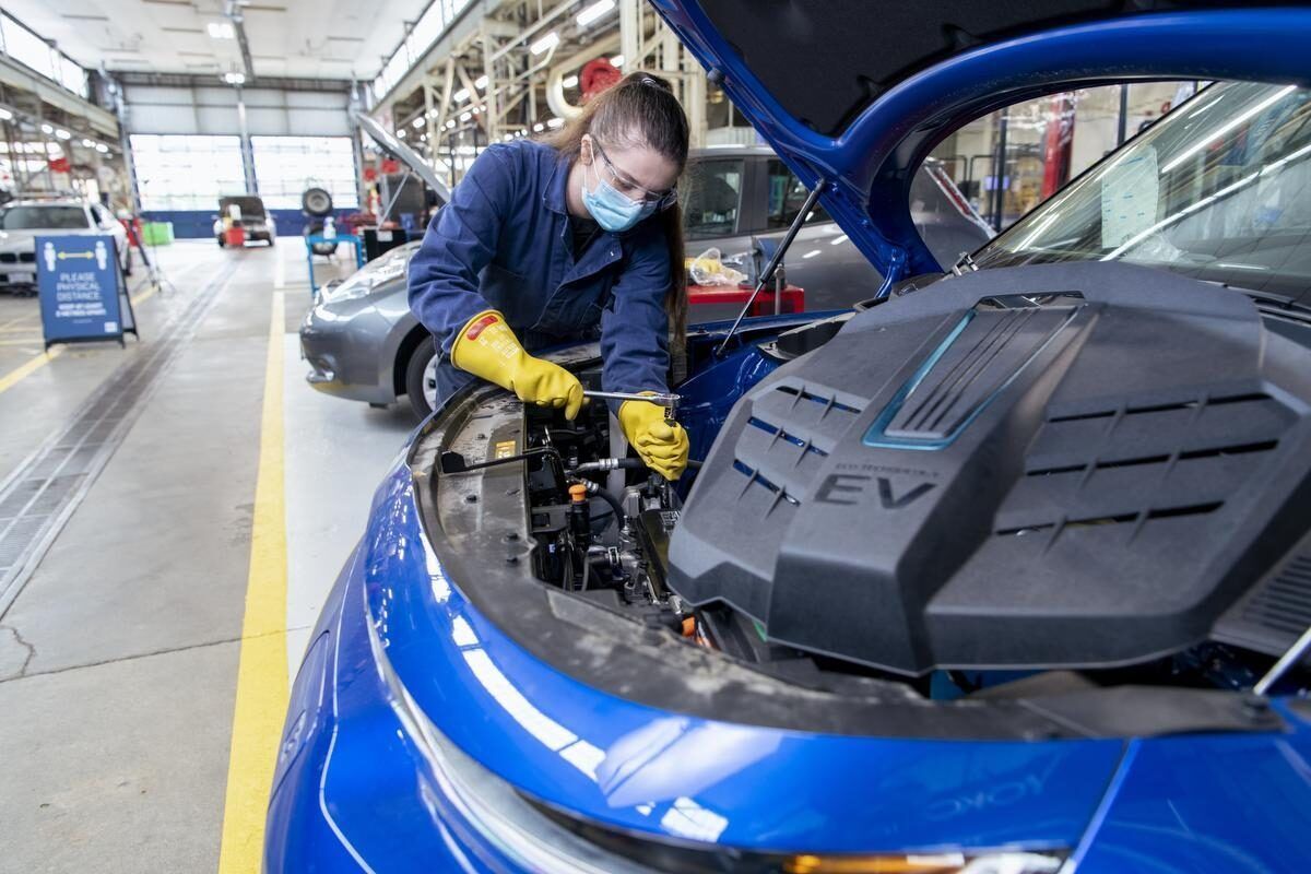 Eine Person, die Handschuhe und eine Maske trägt, arbeitet in einer geräumigen, gut beleuchteten Garage an der Batterie eines Elektrofahrzeugs.
