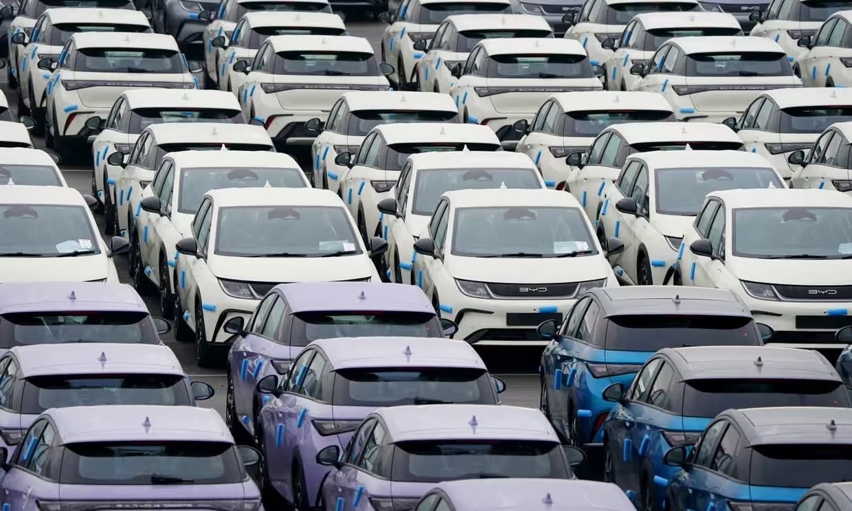 Un gran estacionamiento lleno de filas de autos idénticos, blancos y azules, vistos desde arriba, muestran una disposición uniforme y organizada.