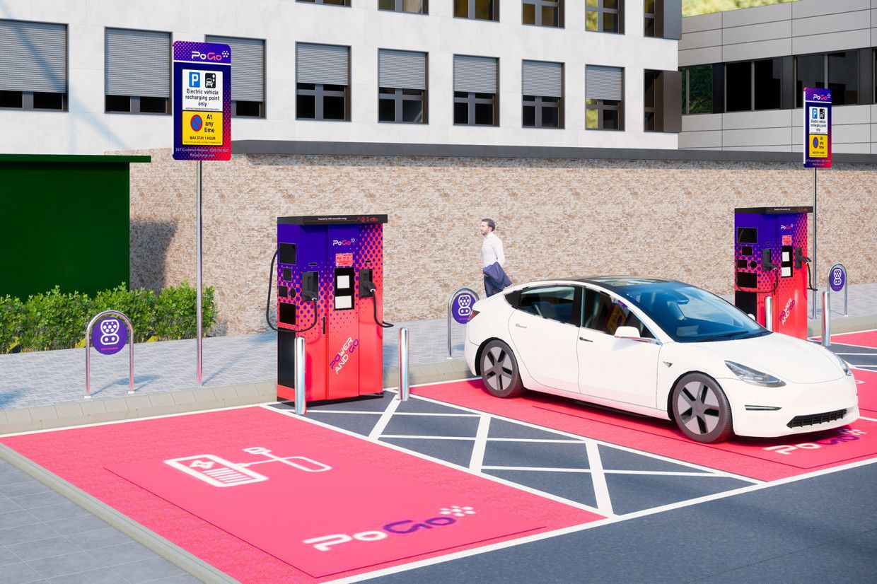 Un automóvil eléctrico se carga en una estación de carga PoGo de color rojo y morado vibrante en un estacionamiento, con un edificio al fondo.