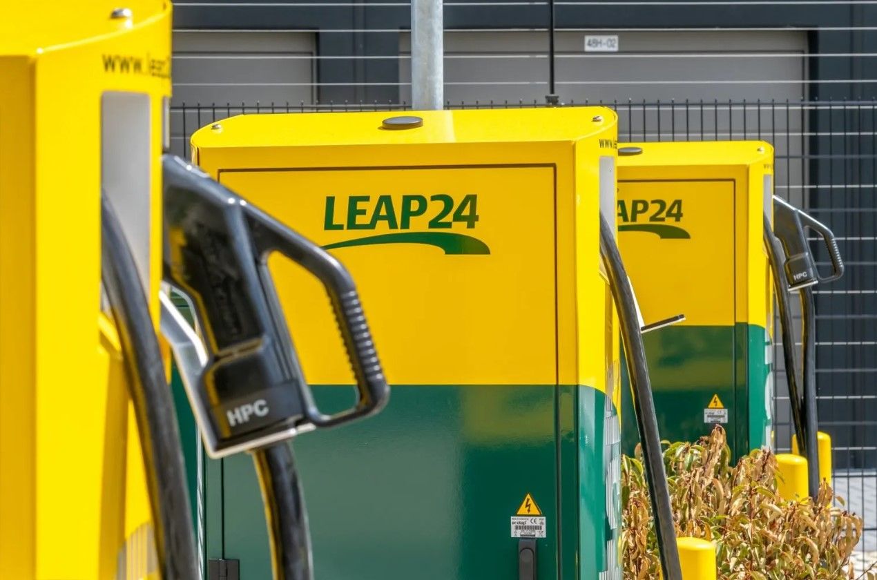 Yellow and green Leap24 fast electric vehicle chargers in front of a black fence