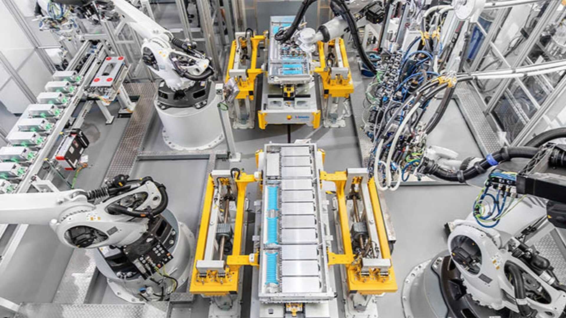 Brazos robóticos que ensamblan paquetes de baterías en una instalación de fabricación avanzada con maquinaria automatizada y sistemas de transporte.