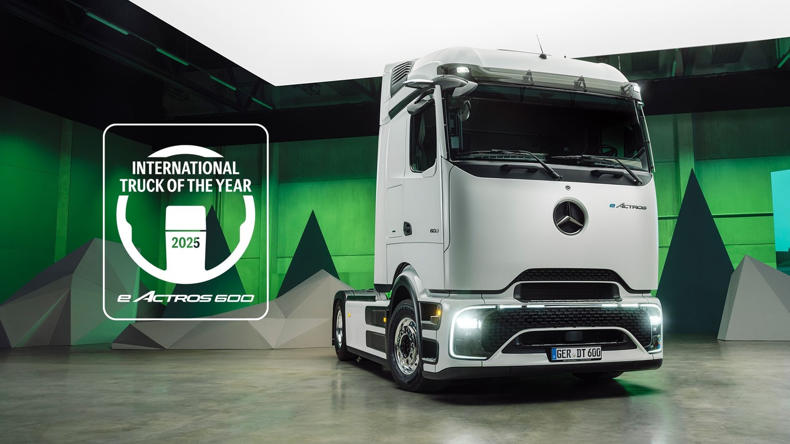 Camión Mercedes-Benz eActros 600 blanco en una sala iluminada con luz verde, galardonado con el premio «Camión Internacional del Año 2025».
