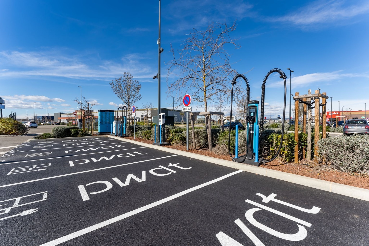 Estación de carga para vehículos eléctricos Powerdot en un estacionamiento con cielo azul claro y tráfico mínimo.