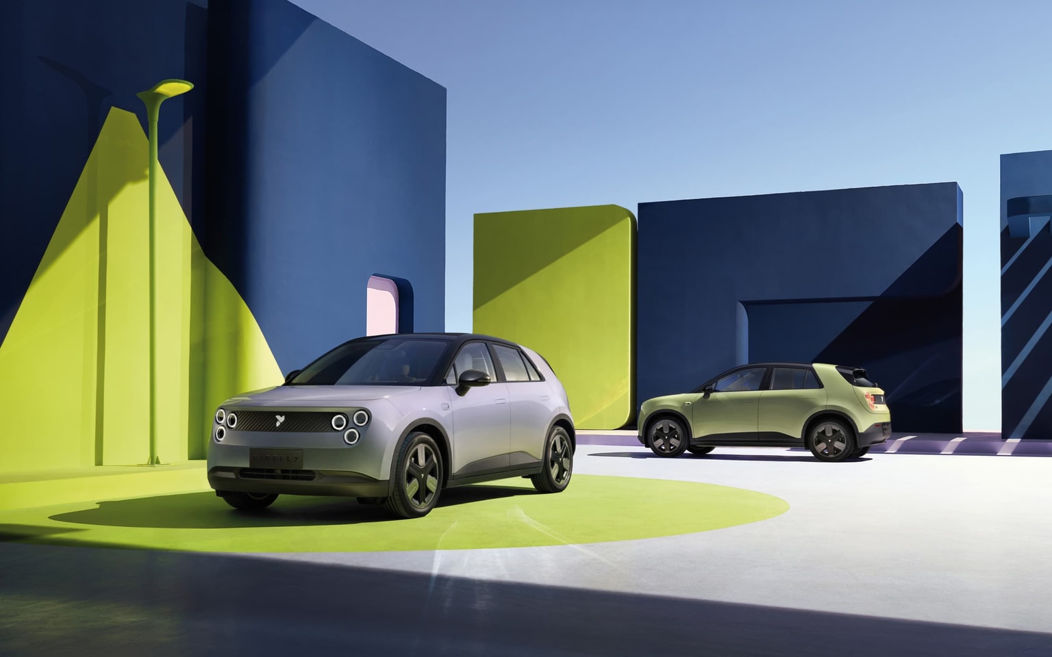 Dos coches eléctricos modernos aparcados sobre un fondo geométrico vibrante con llamativas formas azules y verdes bajo un cielo despejado.