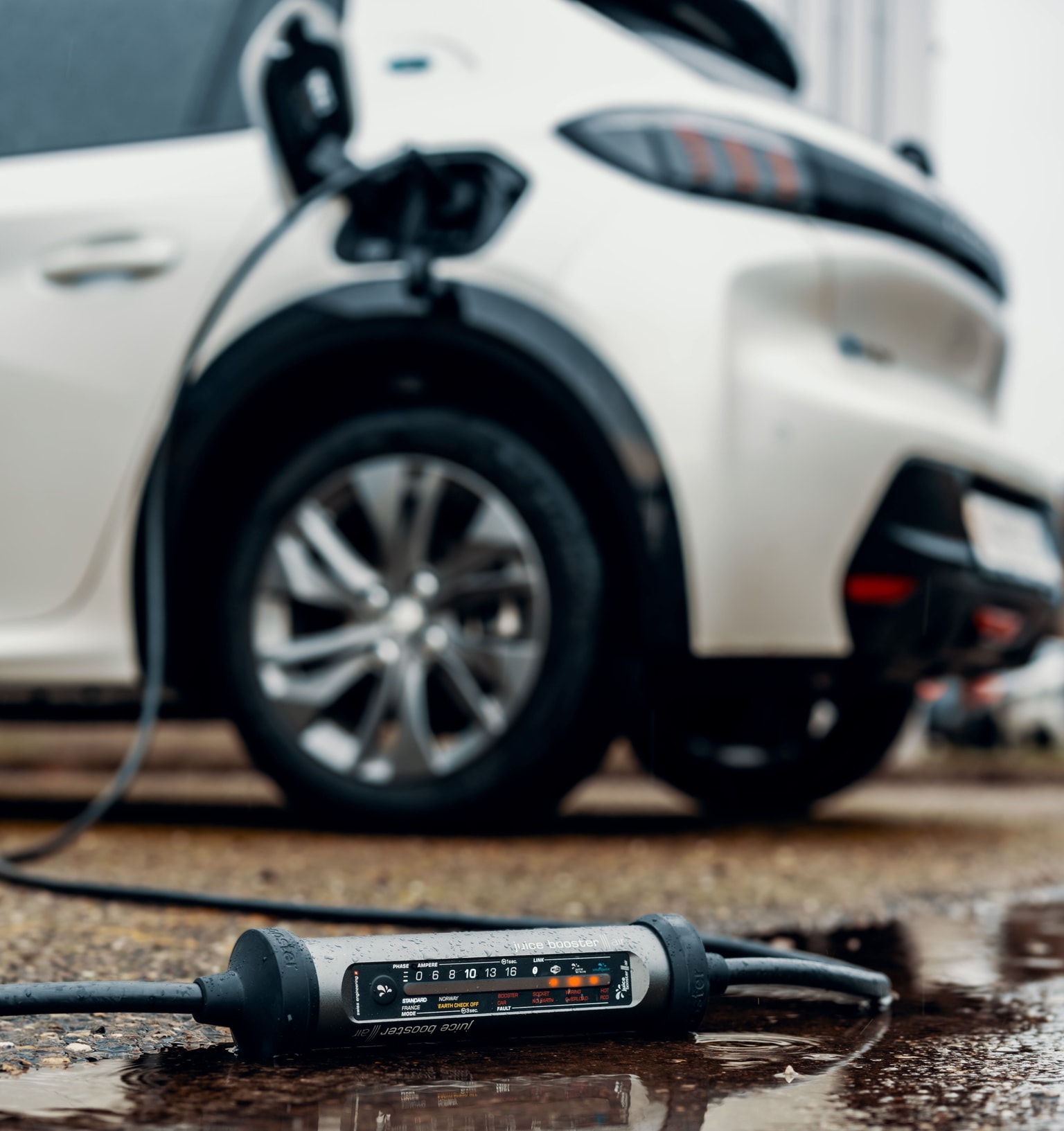 Primer plano de un automóvil eléctrico cargándose, con el foco puesto en el cable de carga y el indicador, estacionado sobre una superficie mojada.