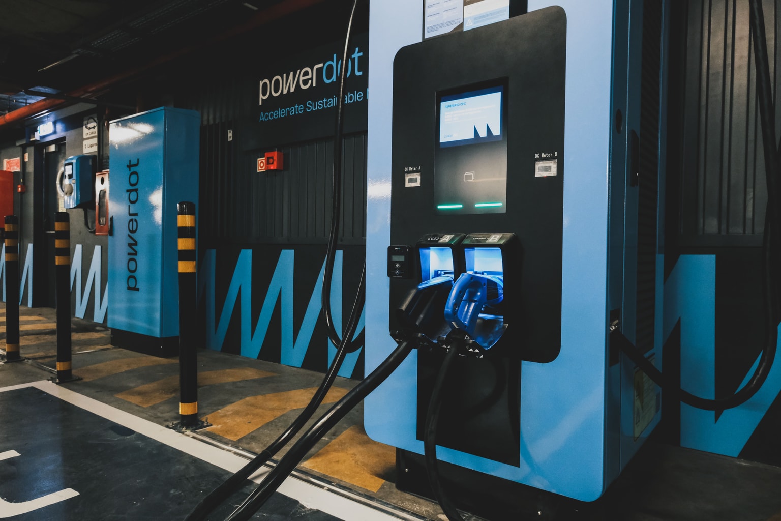 Estaciones de carga de vehículos eléctricos Powerdot con detalles azules y pantallas digitales en un área de estacionamiento.