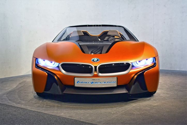 Futuristischer orangefarbener Sportwagen mit schlankem Design, beleuchteten Scheinwerfern und einem markanten BMW-Logo, ausgestellt in einem Showroom.
