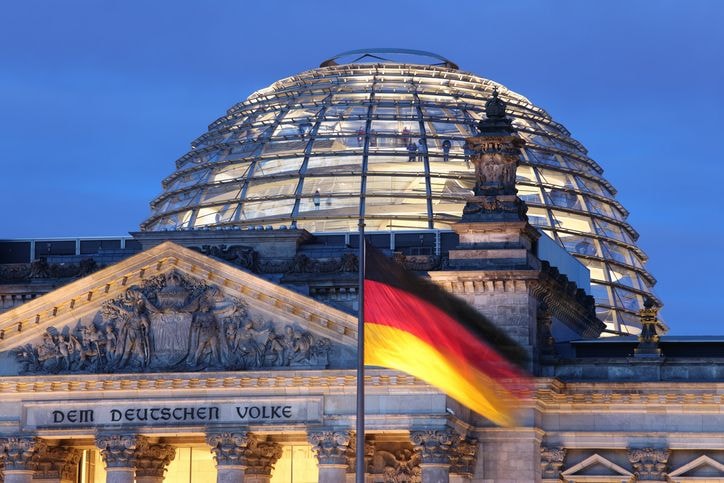 The Reichstag building with its glass dome illuminated at night, a German flag waving in the foreground.