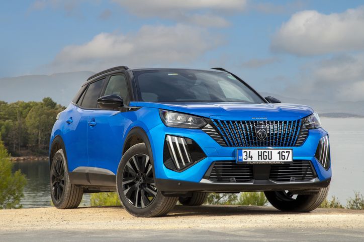 Um SUV azul vibrante estacionado ao ar livre com um cenário pitoresco de árvores e um lago, sob um céu parcialmente nublado.