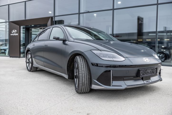 Ein elegantes graues Elektroauto von Hyundai, das an einem klaren Tag vor einem Autohaus mit Glasfassade geparkt ist.