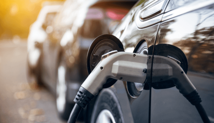 Primer plano de un coche eléctrico cargándose, con un cable de carga conectado. Otros coches aparecen desenfocados al fondo.