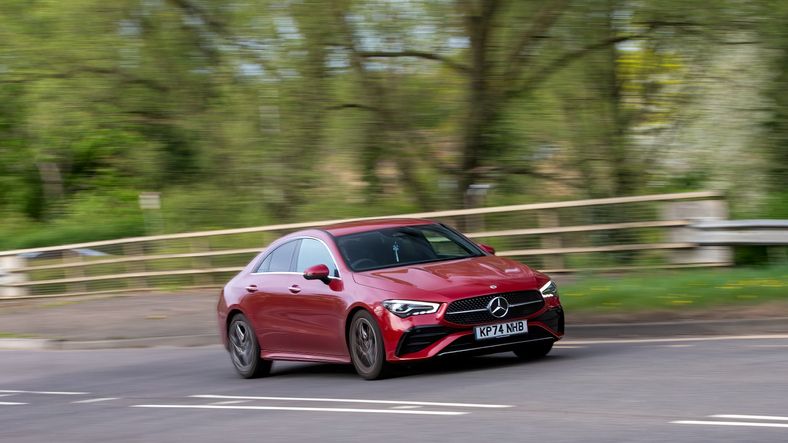 Red Mercedes-Benz car driving on a road with blurred green trees in the background.