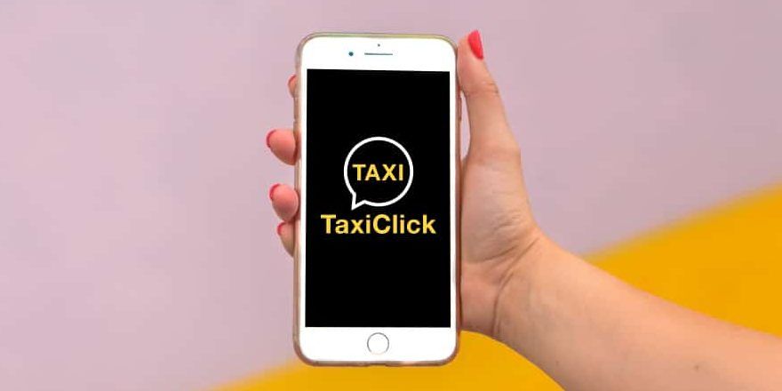 Hand holding a smartphone displaying the TaxiClick app logo on the screen, with a pink and yellow background.