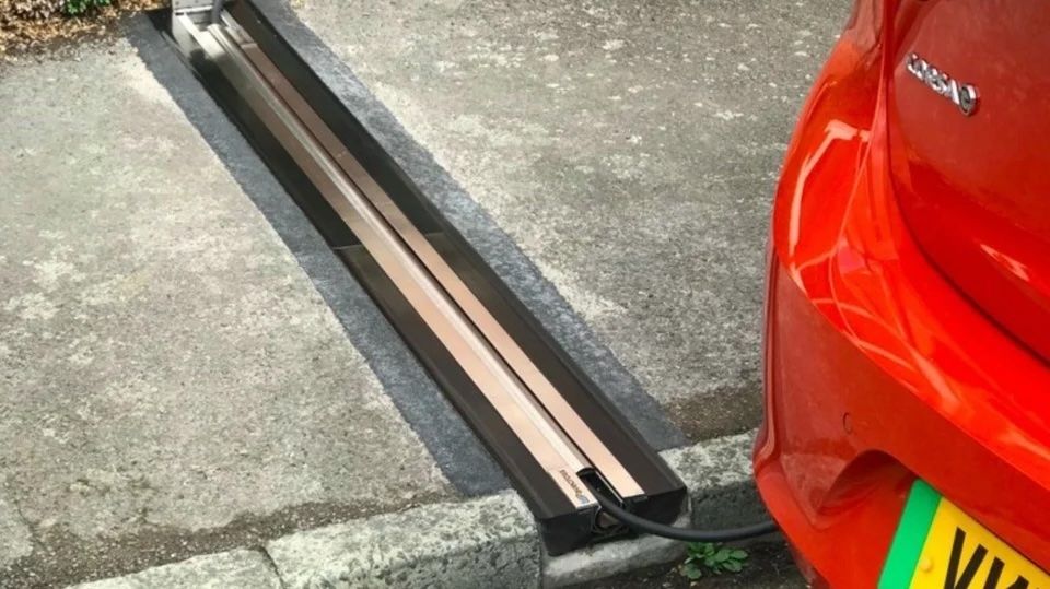 Coche rojo cargándose en una estación de recarga para vehículos eléctricos integrada en el pavimento junto a la acera.